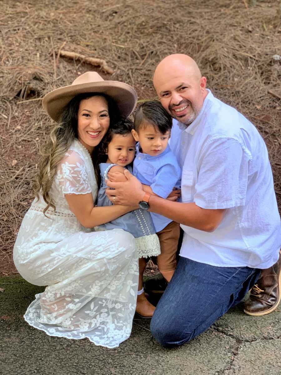 Couple take picture crouching down with two young children between them.