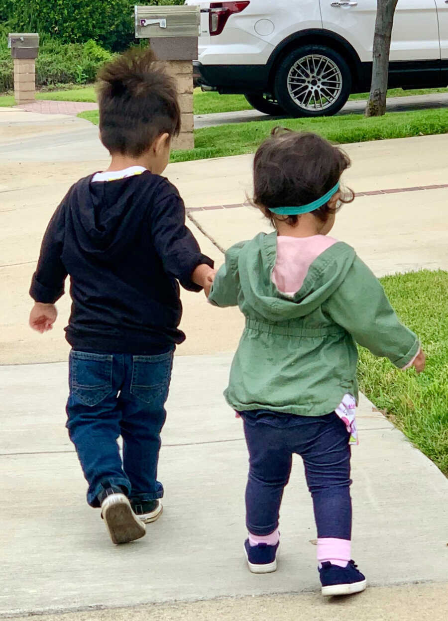 Adoptive brother and baby sister walk together holding hands.