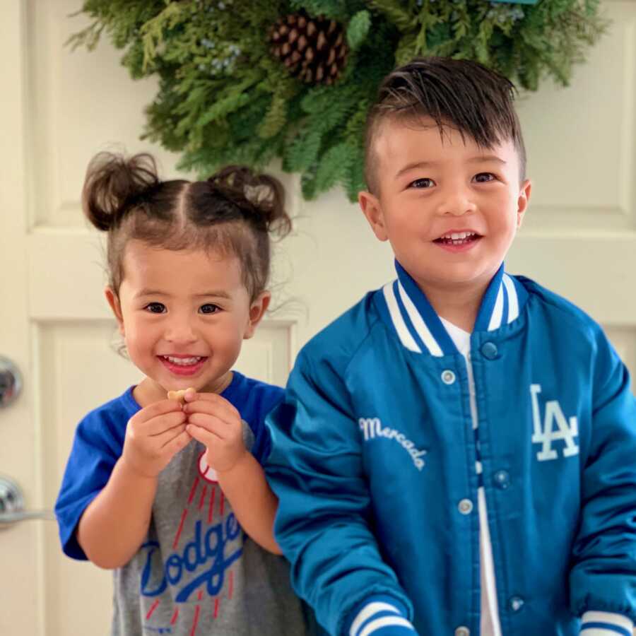 Brother and sister take picture standing next to each other smiling and wearing baseball fan gear.
