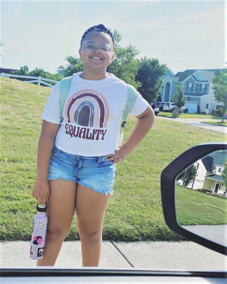 Young black teen girl proudly wears her new shirt and poses with her hand on her hip.