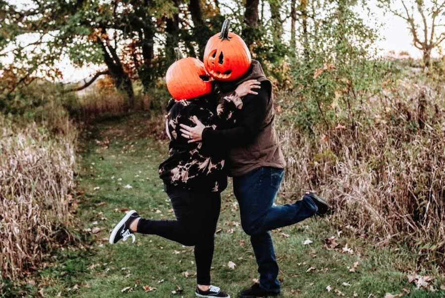 A couple wearing pumpkins of their heads embrace