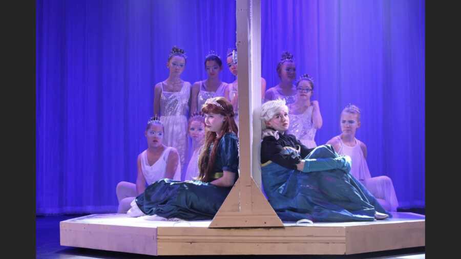 Student actors playing Anna and Elsa from Disney's Frozen sit on opposite sides of a door and sing their parts in an inclusive theatre performance.