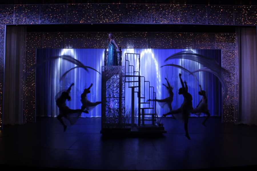 Silhouette of students dancing on stage in an inclusive performance of Disney's Frozen.