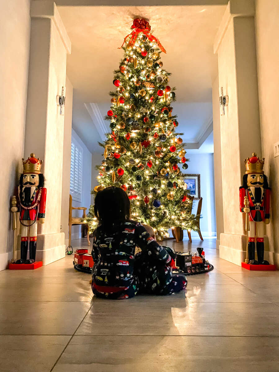 siblings in matching pajamas sit facing tree together