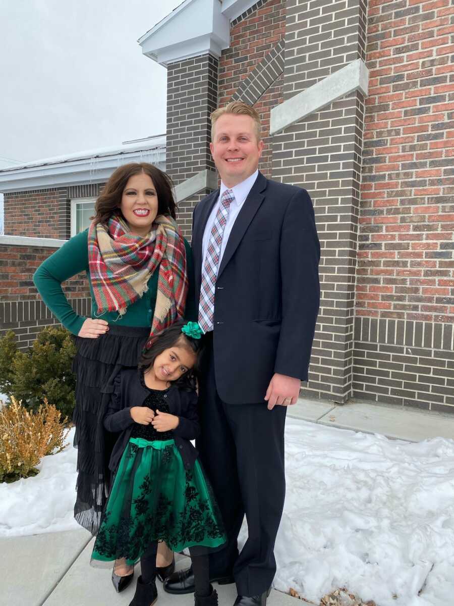 mom and dad stand with daughter in formal attire