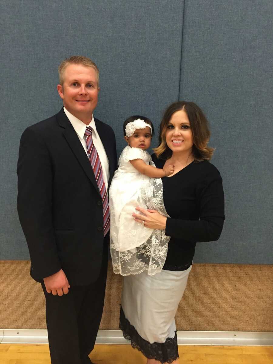 mom and dad hold their baby daughter who is wearing a white dress