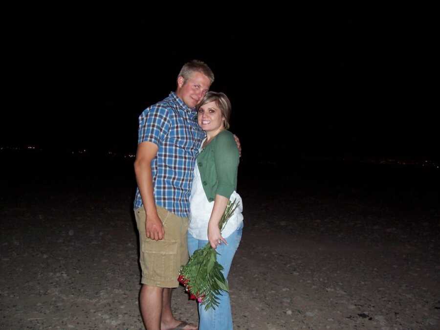 couple stands together, woman holds flowers