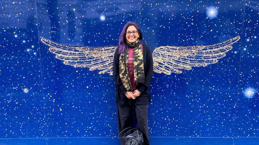 domestic violence survivor standing in front of blue wall with wings painted on it