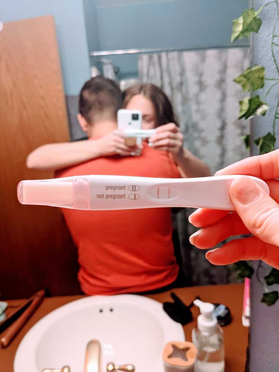 husband and wife hugging with pregnancy test