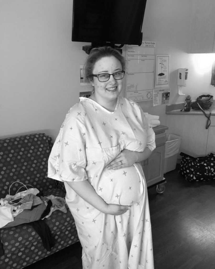 Pregnant woman in hospital gown holds belly as she prepares to deliver her baby.