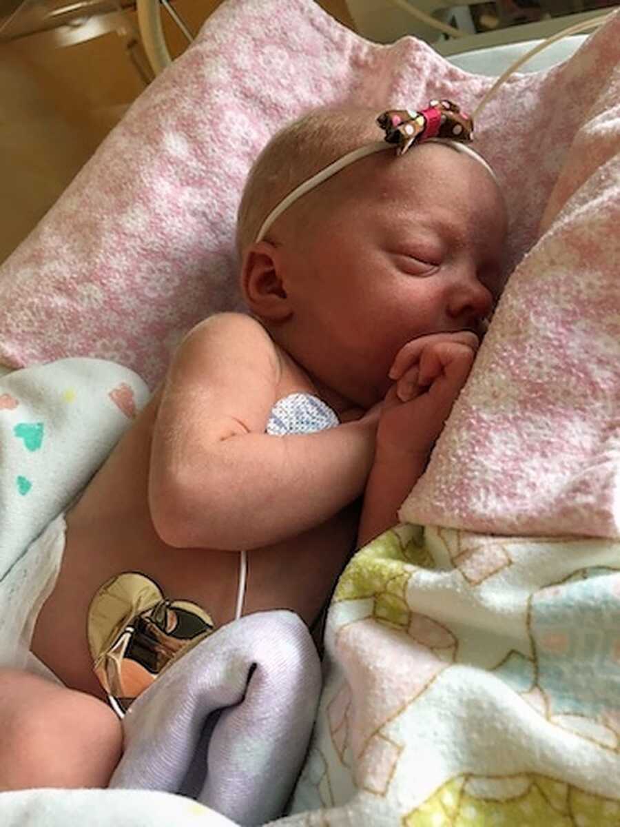 Newborn baby girl lies curled up in blankets at the hospital with monitors hooked up to her.