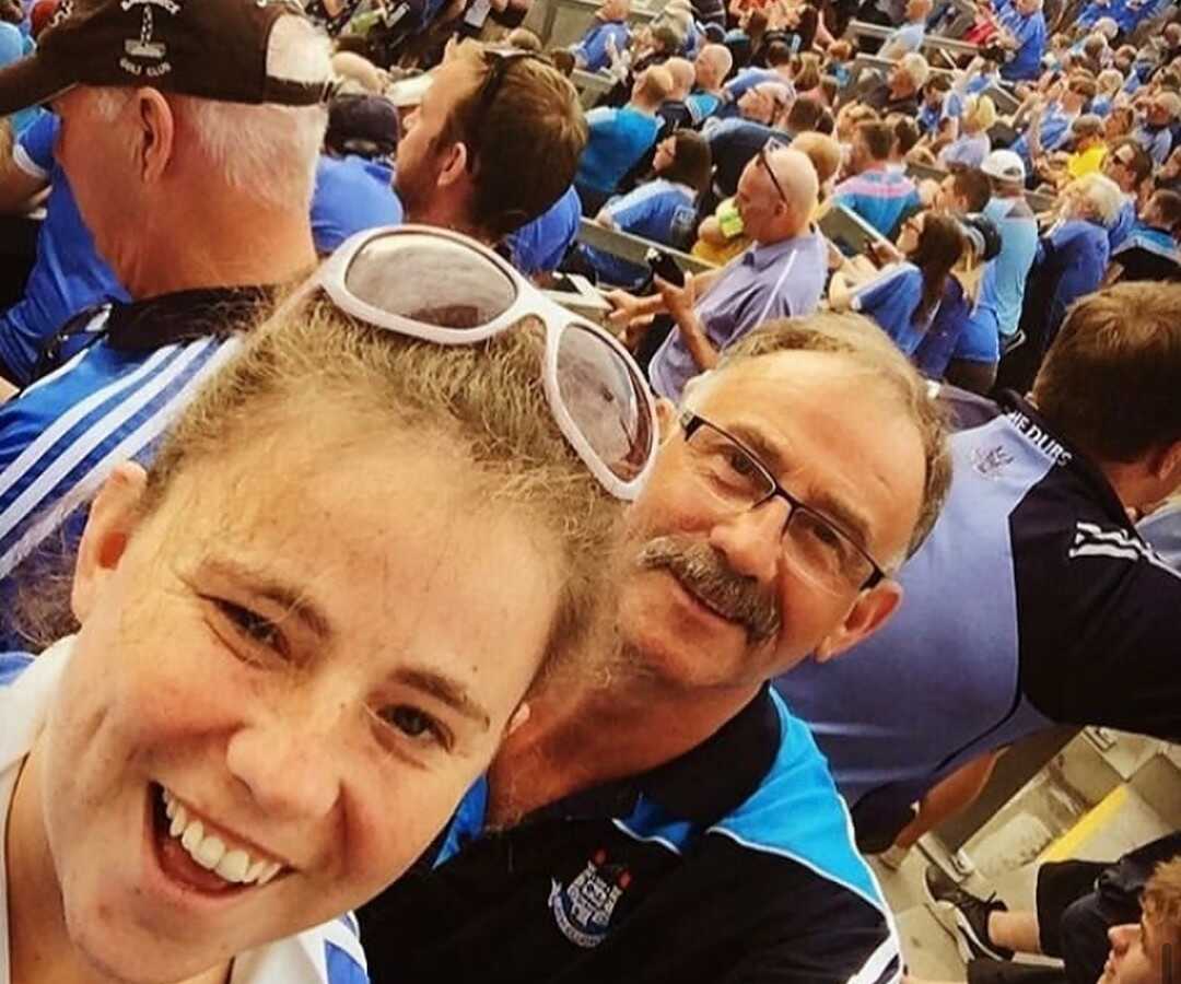 Young woman takes selfie with father at crowded event.