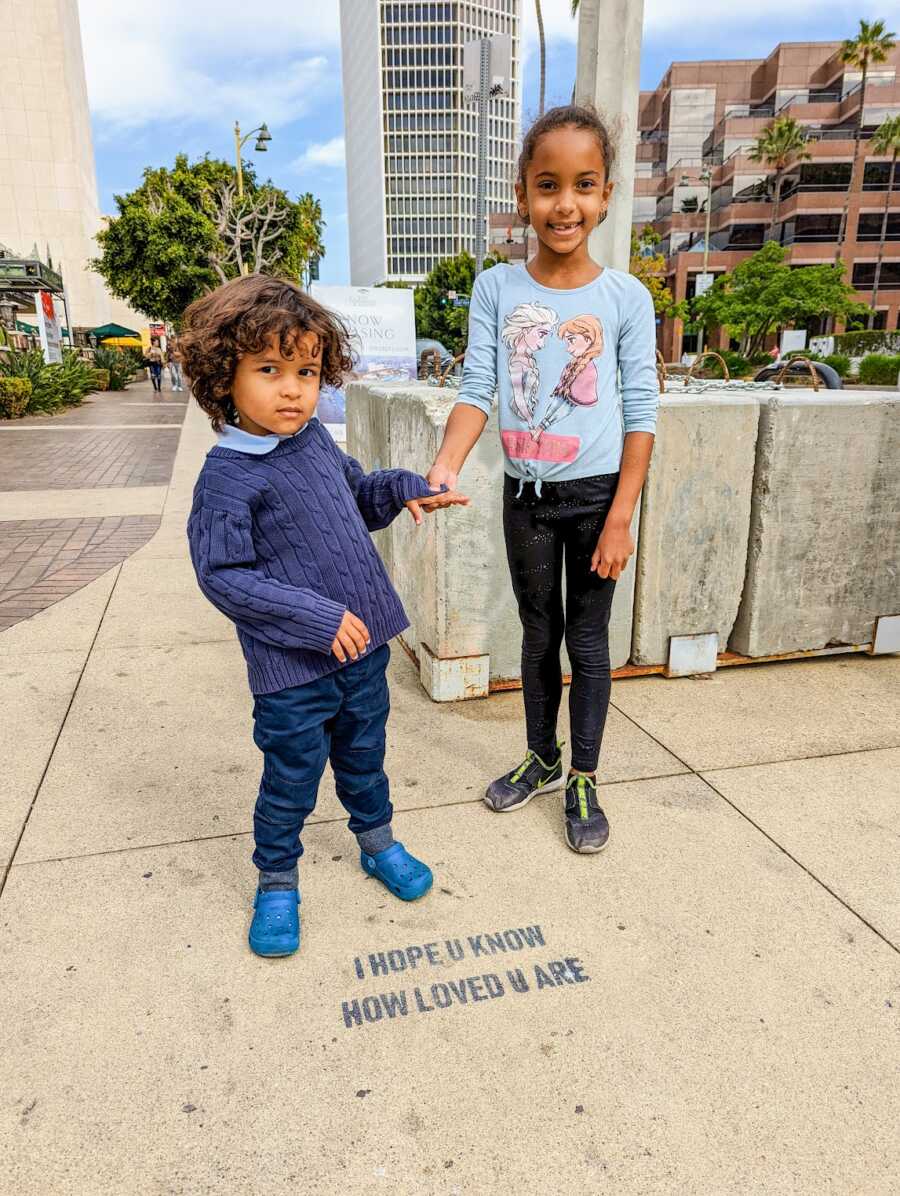 Young girl holding hands with younger, autistic brother