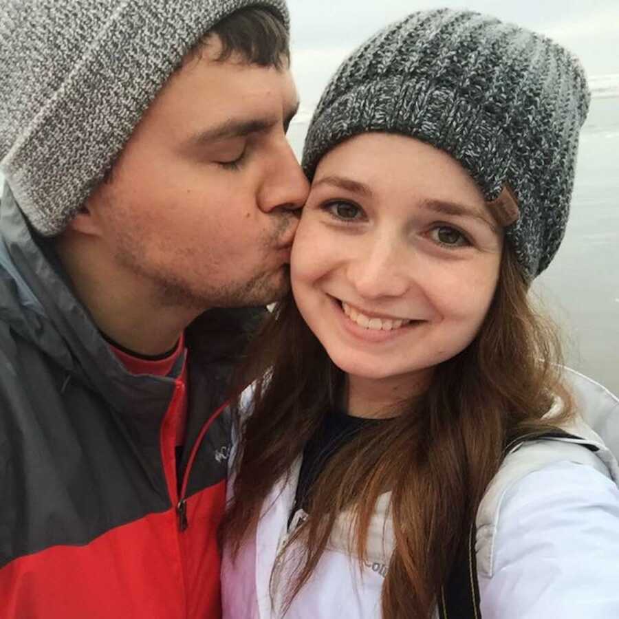 Man kisses woman on the cheek as she smiles for a selfie. 