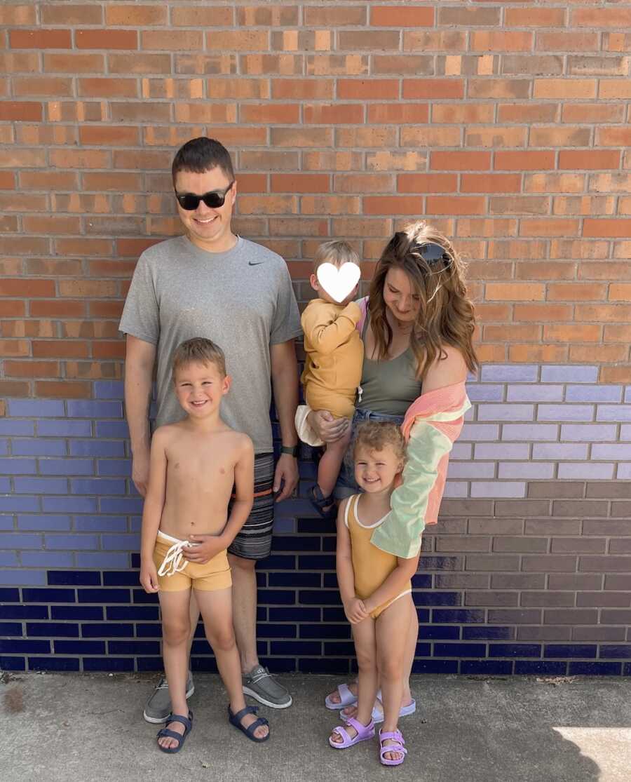 Foster family takes picture in swimsuits in front of colorful brick wall.