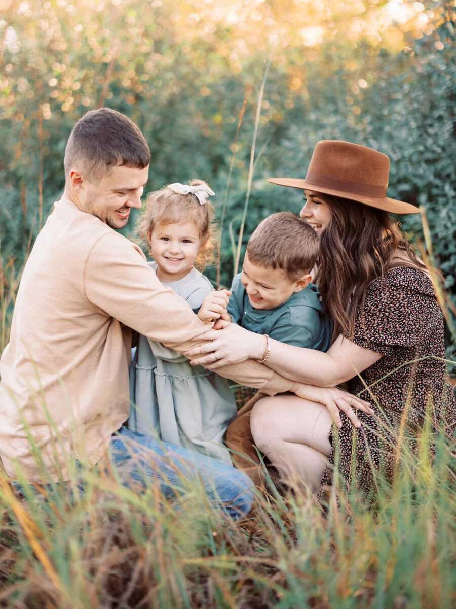 Parents crouch down with arms around son and daughter for family photo.