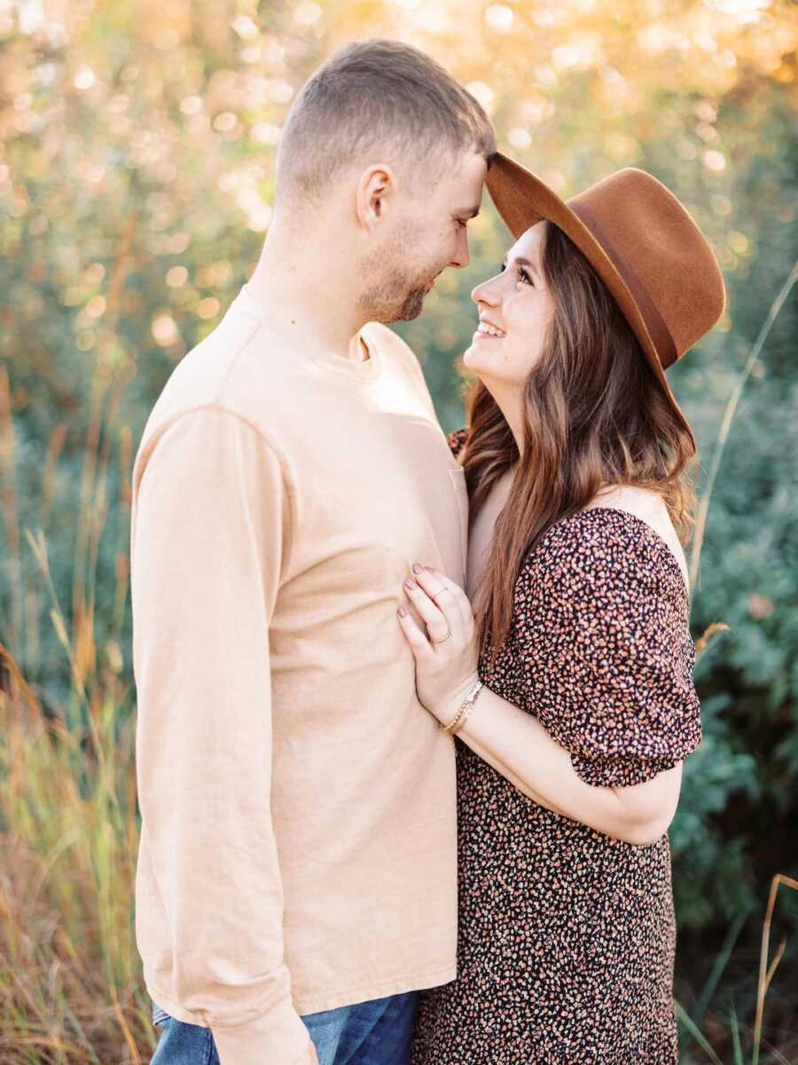 Husband and wife gaze into each other's eyes and smile, while wife rests her hand on husband's chest.