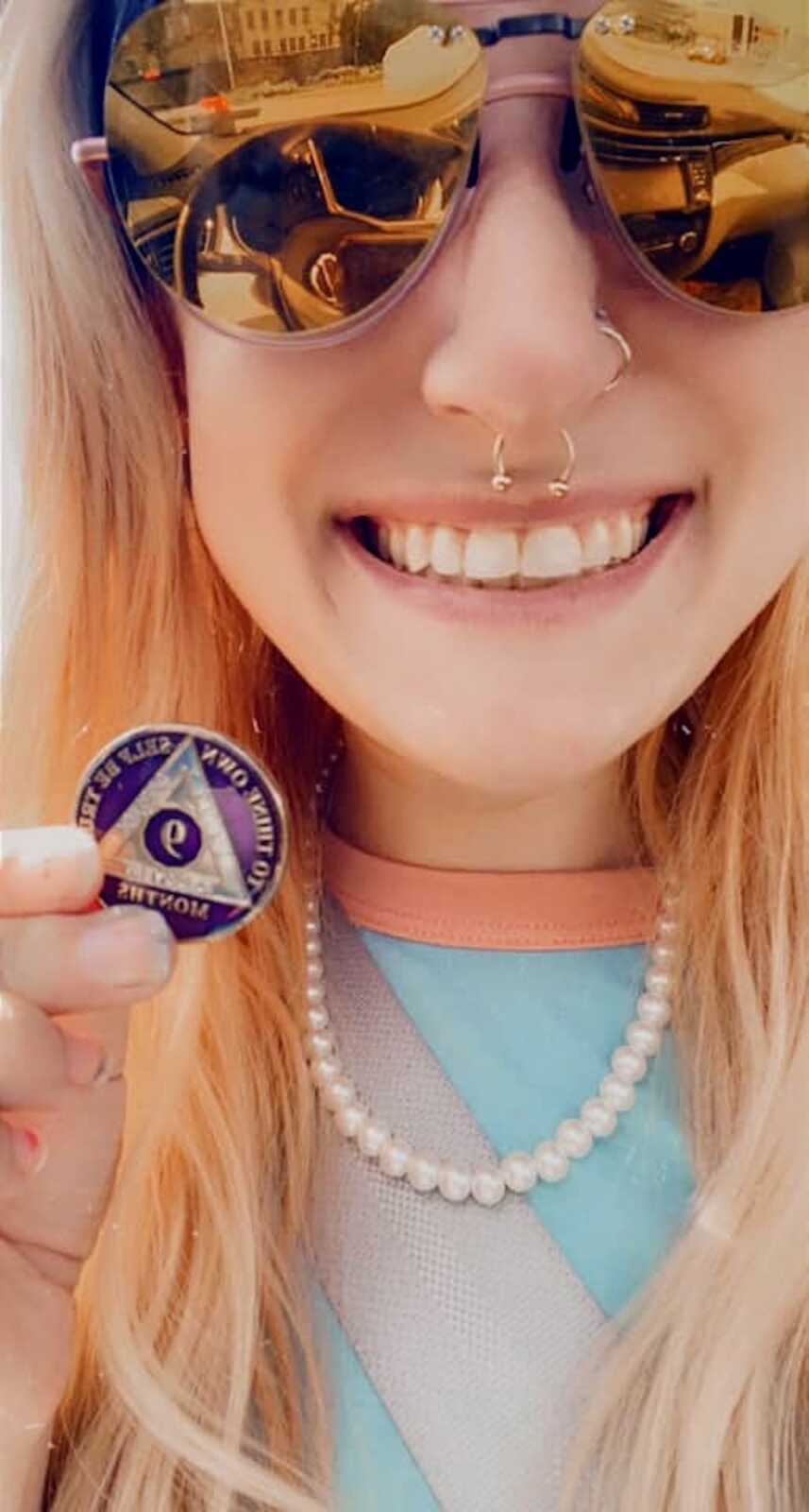 Recovered alcohol addict smiling and holding a '9 months sober' coin