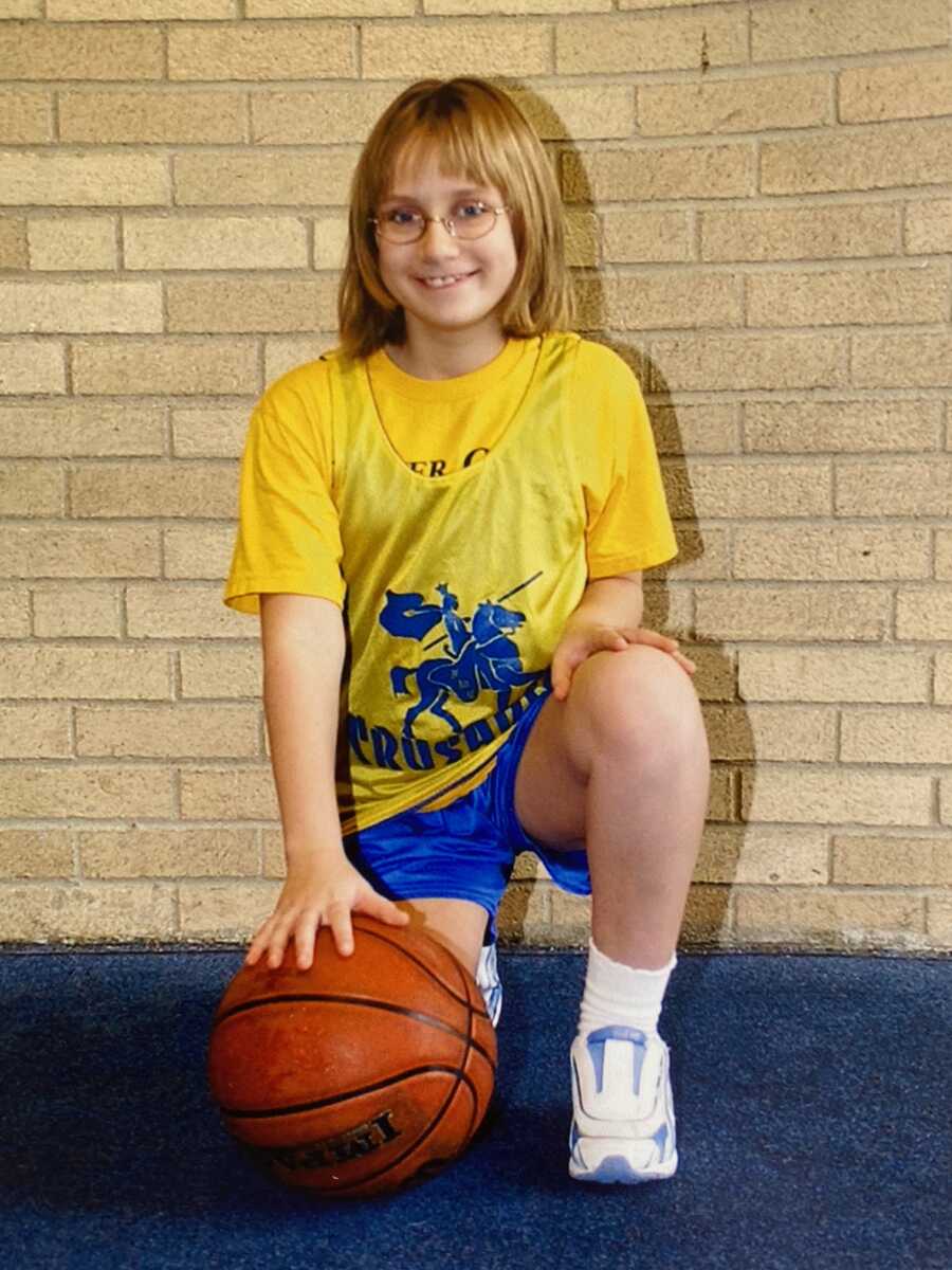 Girl in yellow jersey kneeling with a basketball