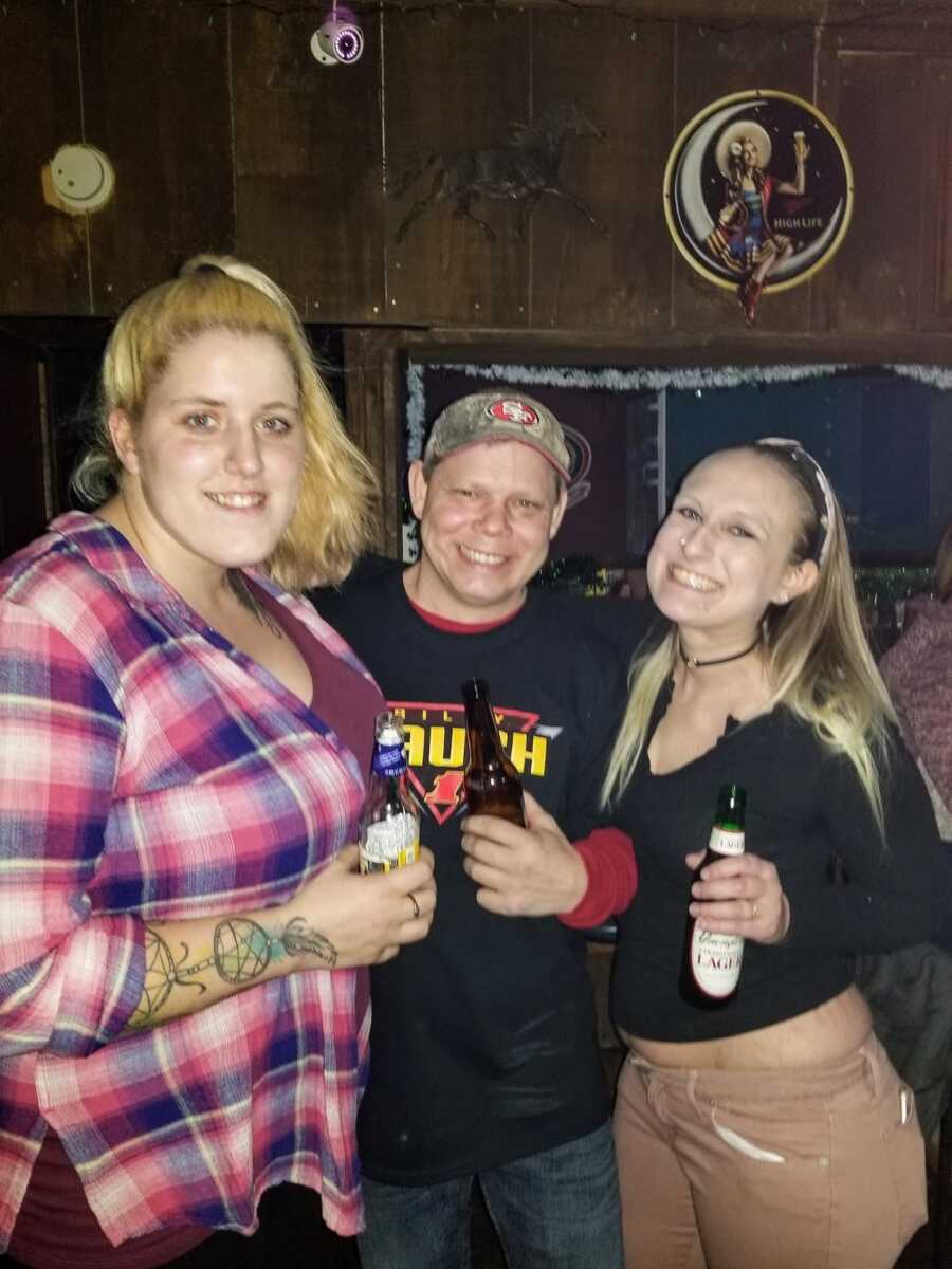 Two women and a man at a bar holding beers