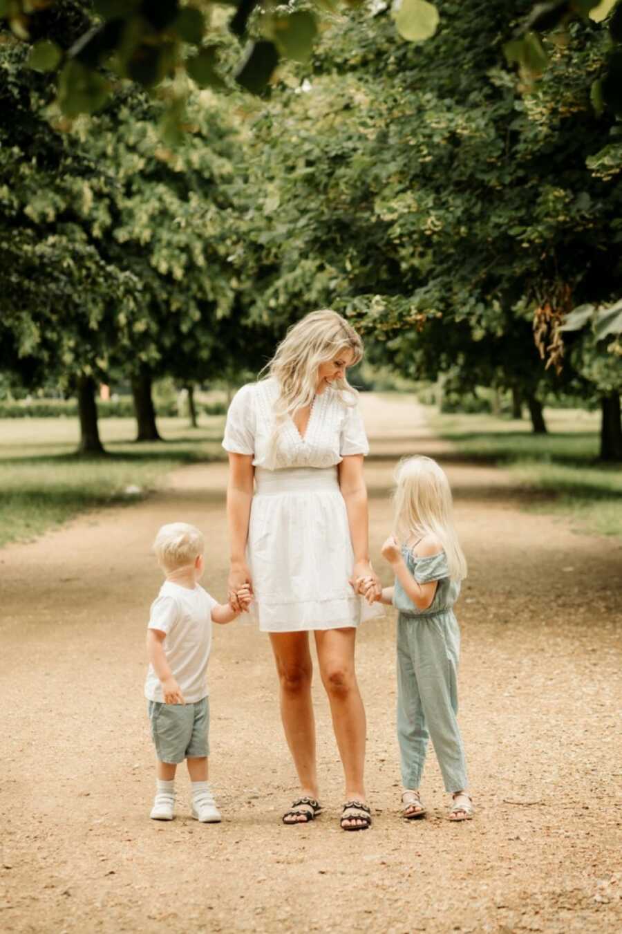 mom holding her kids' hands while beneath the trees
