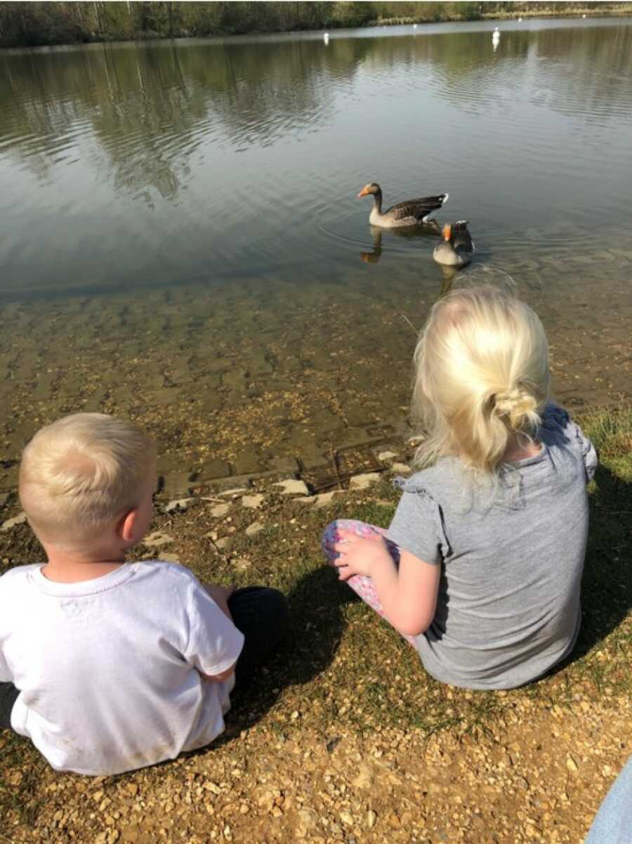 kids sitting on the ground looking at the ducks