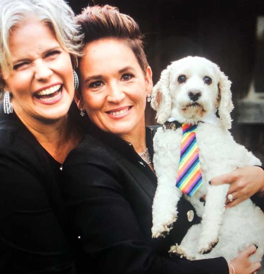 Wives smiling together, one holding their white dog
