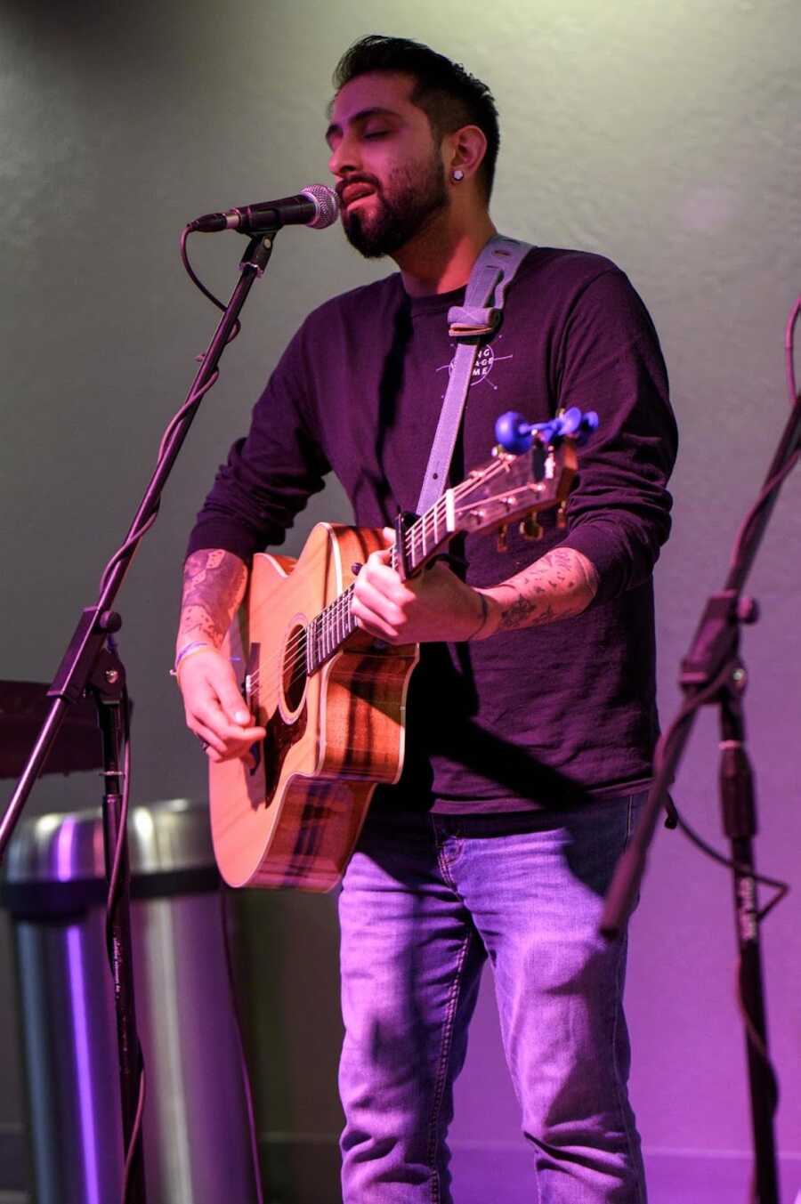 Man playing acoustic guitar on stage and singing into microphone