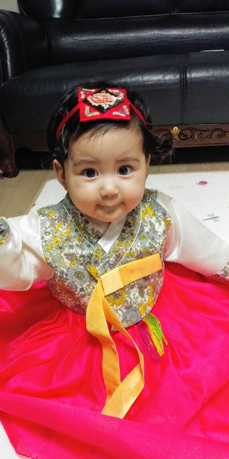 Korean baby girl sits on the floor in her traditional clothing.