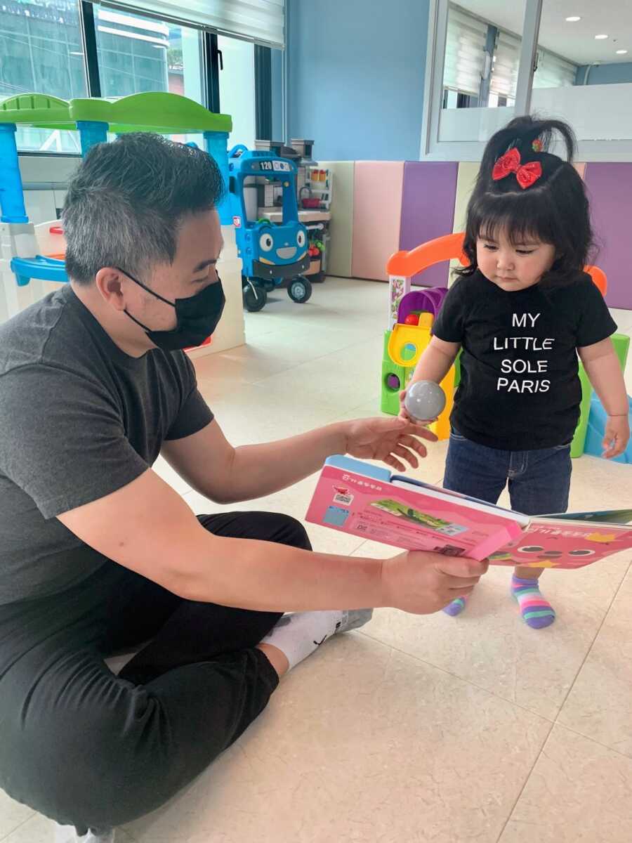 Dad holds out a book for Korean baby girl they are adopting.