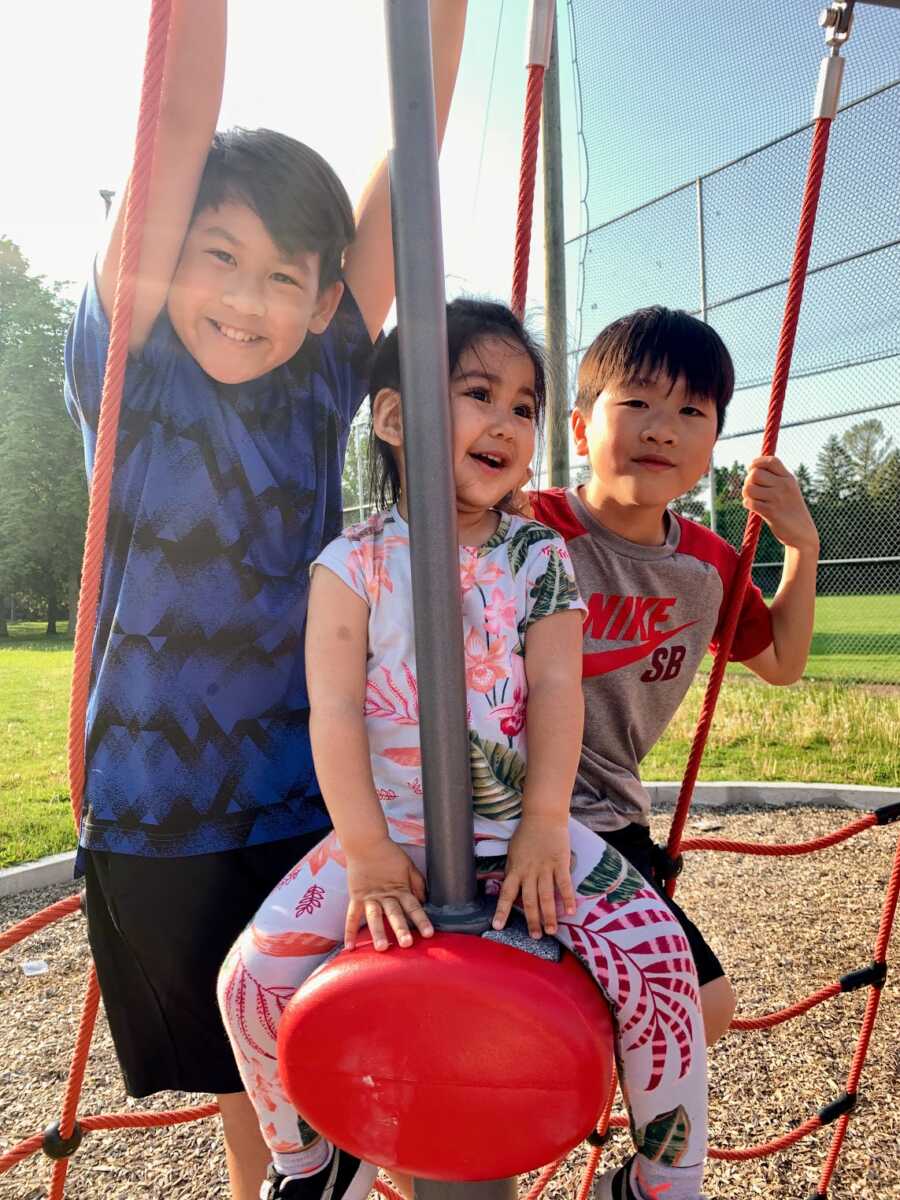 Adopted daughter on playground equipment with her older brothers