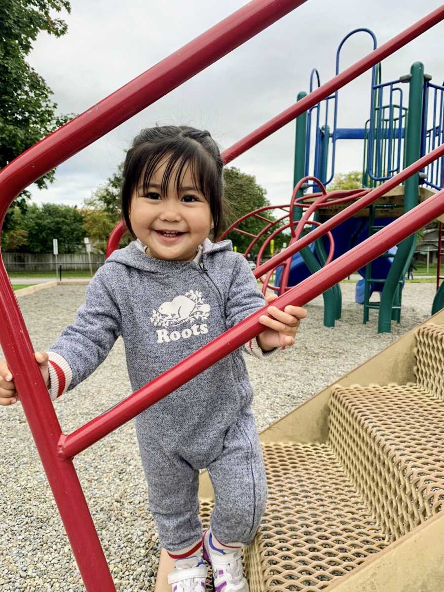 Adopted girl standing on playground stairs in roots onesie