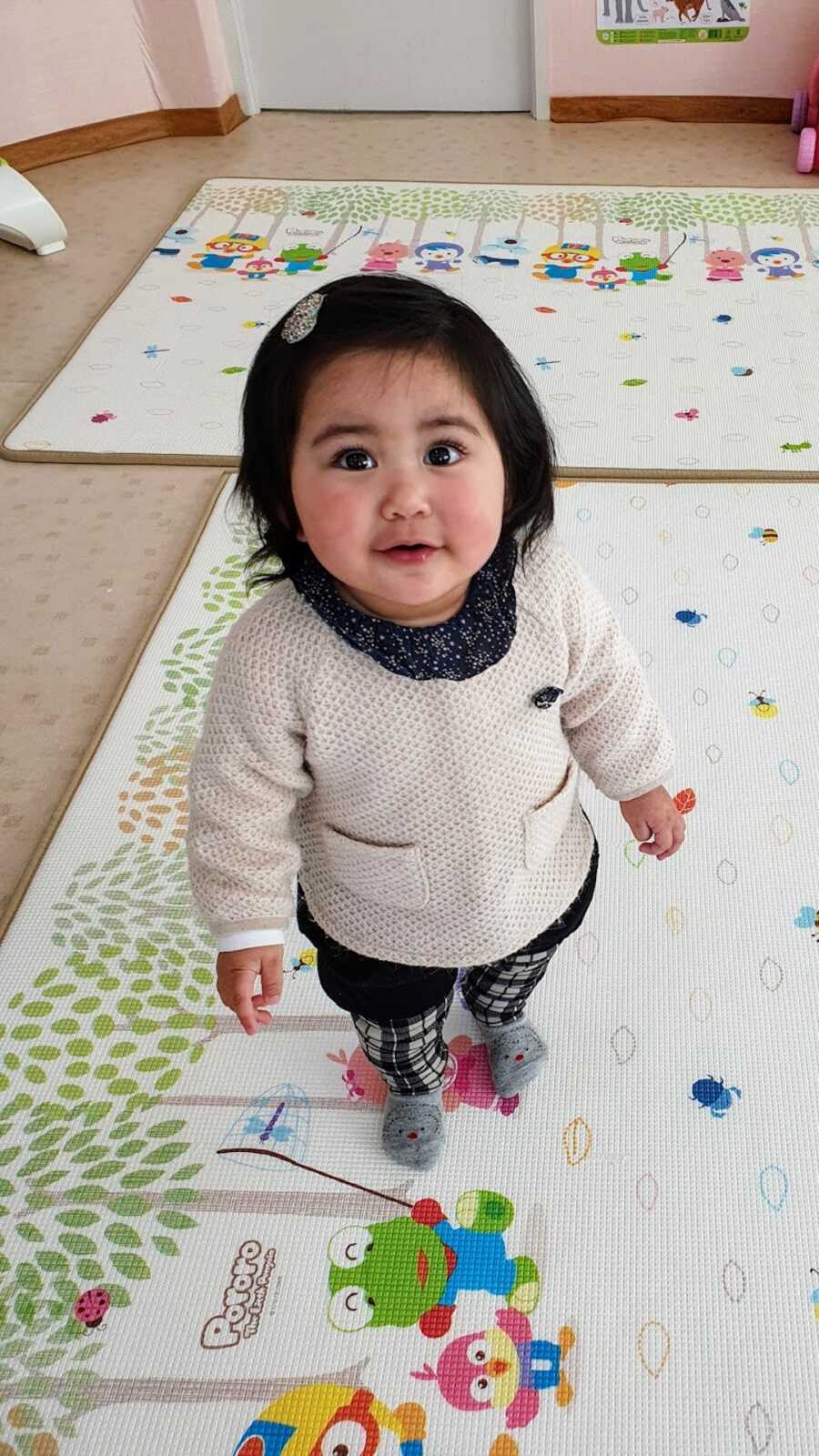 Adopted girl standing on a play rug