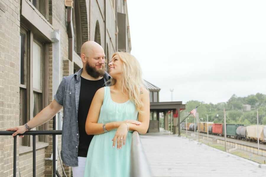 Young couple lovingly gaze at each other in engagement picture at train station.