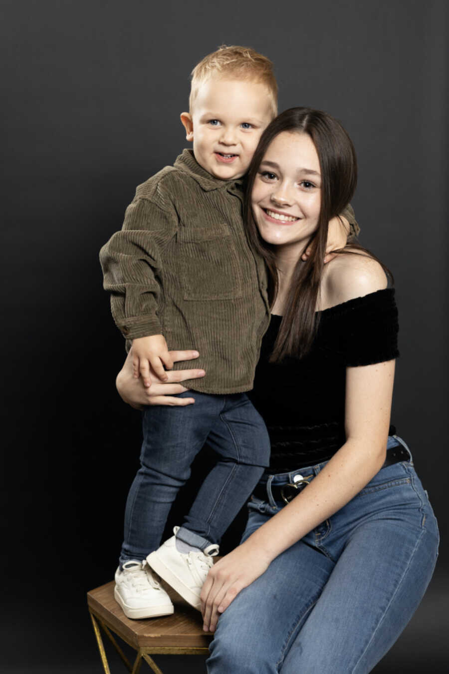 Teenage adopted sister takes picture wrapping arm around baby brother.