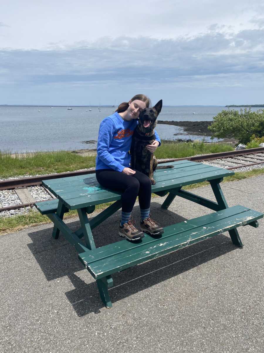 Handler resting her head on service dog sitting on top of a table 