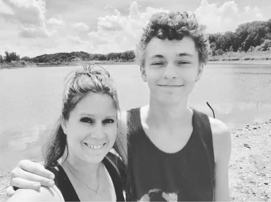 Son rests arm around mom's shoulder as they take a selfie at the lake.