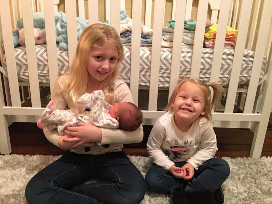 Sisters sitting in front of crib, oldest one hold their baby half sister
