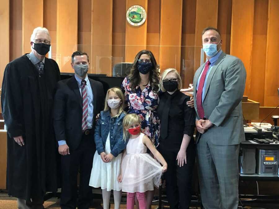 Mother at court with stepdaughters, daughter, and court members following successful adoption trial 