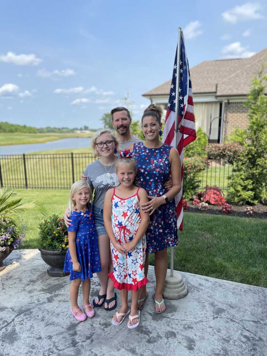 Family standing in front of American flag during Fourth of July