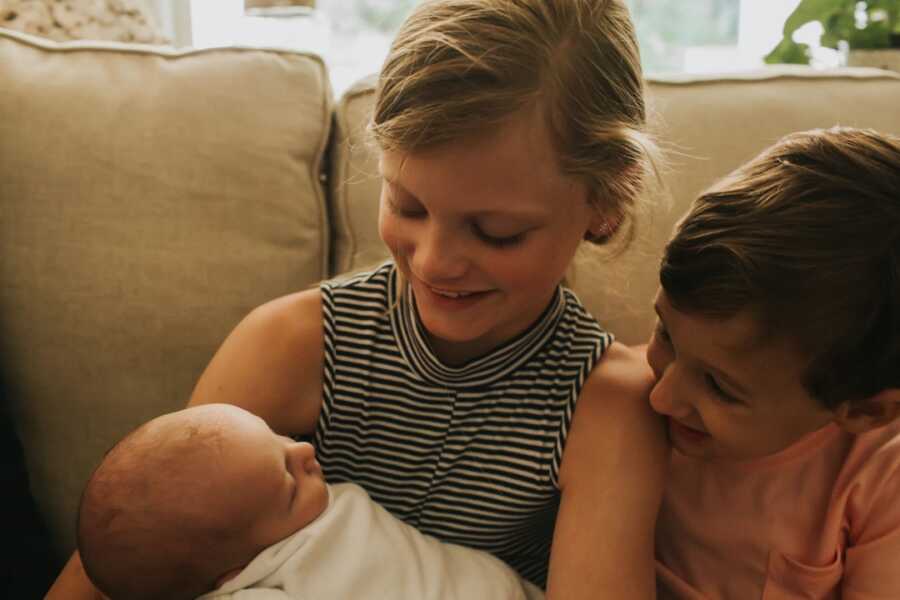 stepdaughter and step brother sit together and hold new born brother 