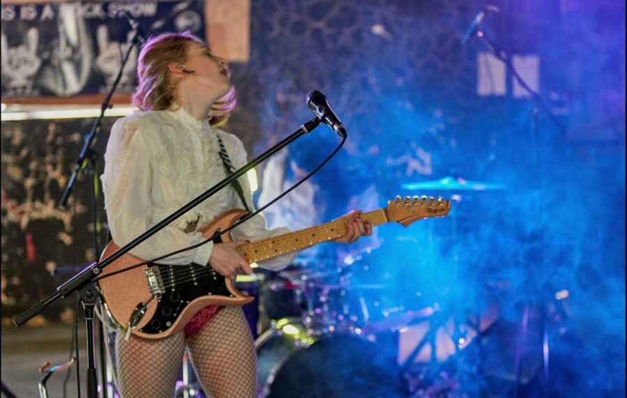 Person in fishnets on stage playing electric guitar