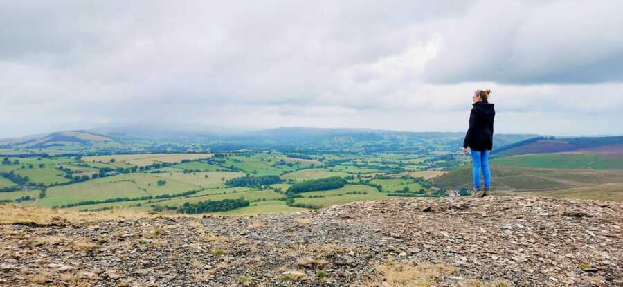 woman standing on mountain looking out at fields