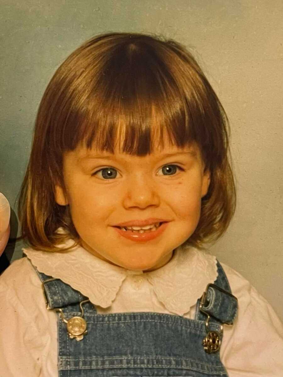 autistic girl smiling in blue overalls