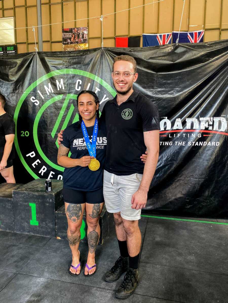 Aboriginal woman with gold medal standing with coach at powerlifting contest 