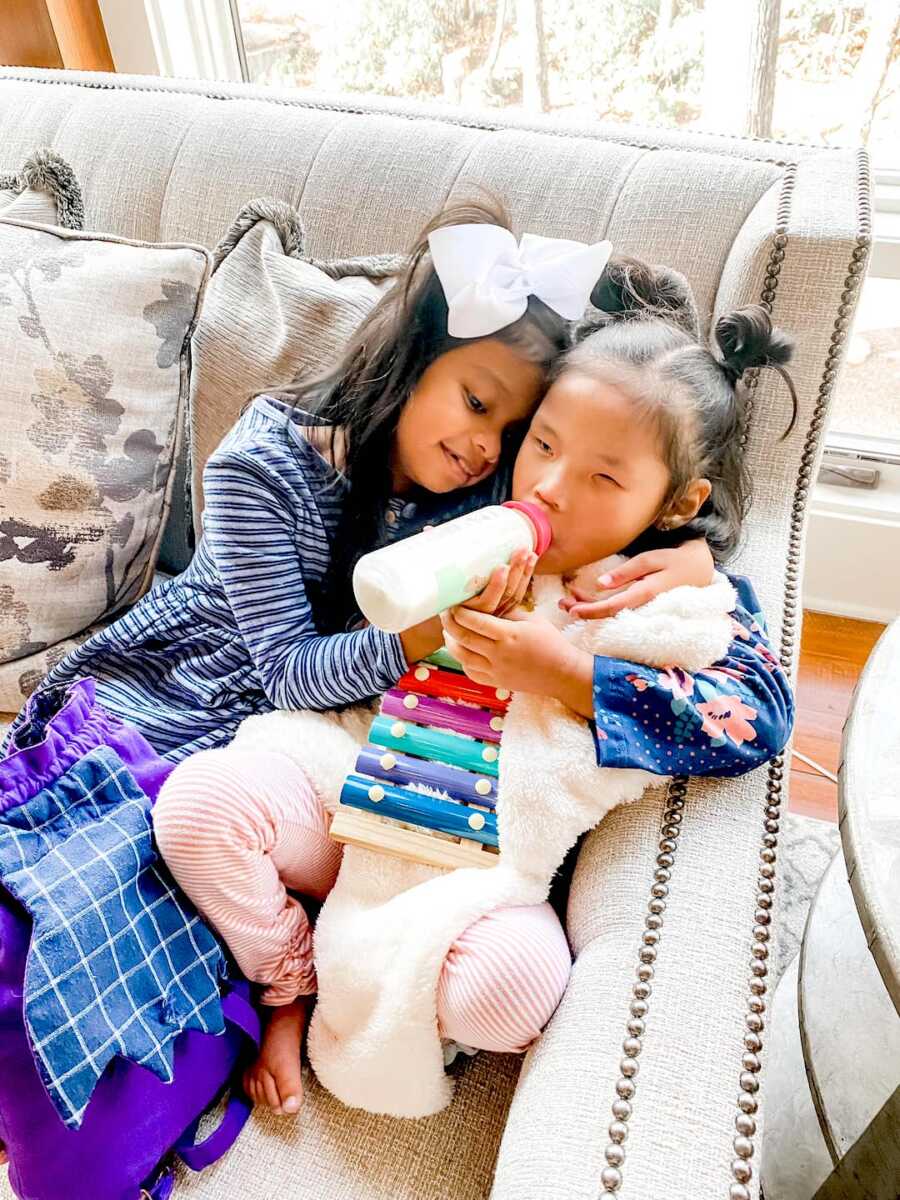 two special needs adopted daughters sit together, one feeds the other