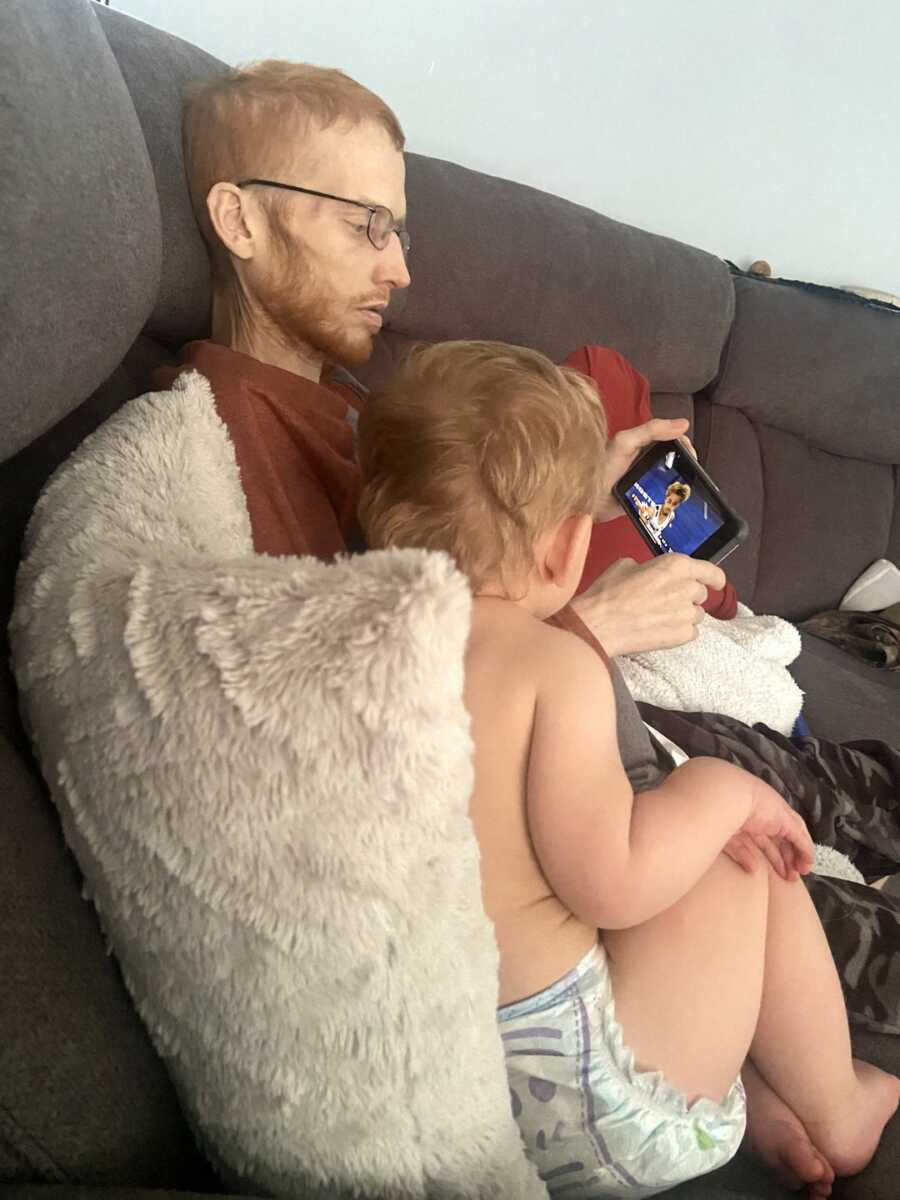 son sits next to father on the couch looking at video on phone