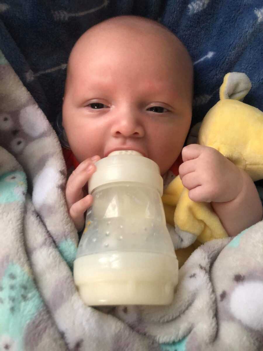 baby lays with blankets while drinking a bottle