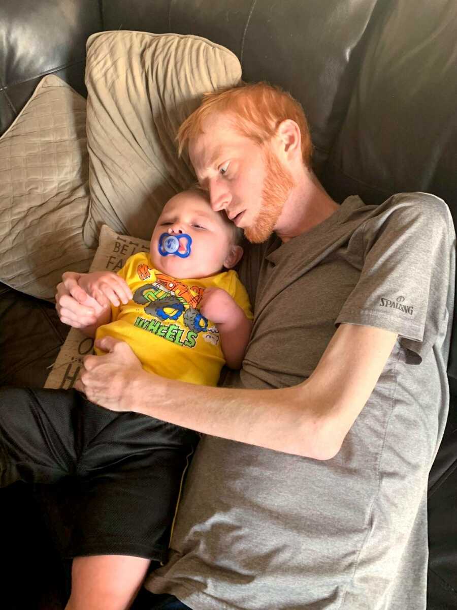 dad holds onto his son while they are laying on couch