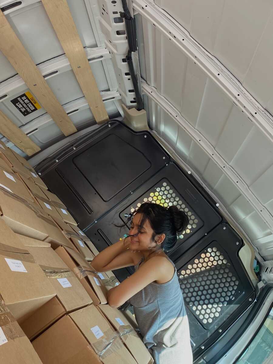 Teen girl rests elbows on packaged boxes of books being delivered to children with cancer.